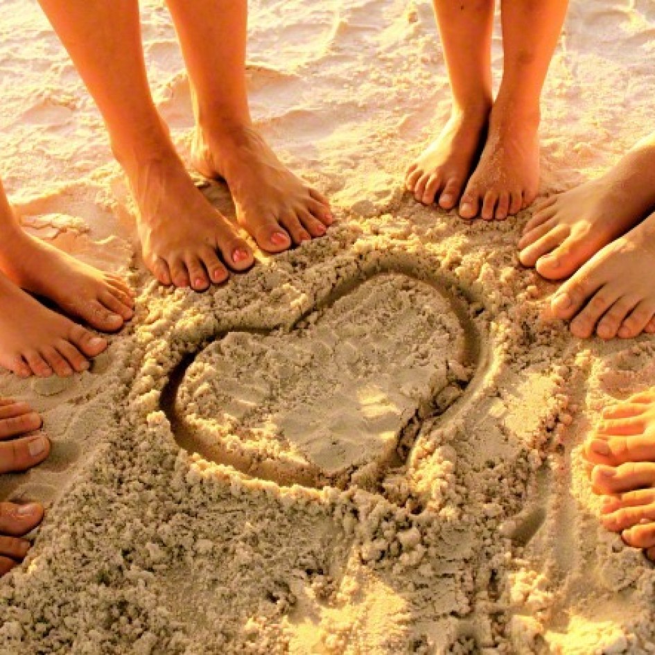 circle of feet on beach with heart
